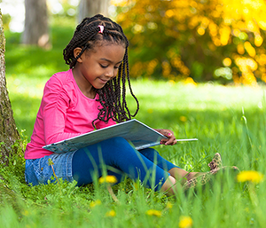 Kindersprache: Aufgabe von Kinderbetreuungseinrichtungen ist es, Kinder gemäß ihrem individuellen Sprachentwicklungsstand in ihrem Spracherwerb zu unterstützen / Clipdealer/ Barmherzige Brüder Mädchen sitzt unter Baum und schaut in ein Buch